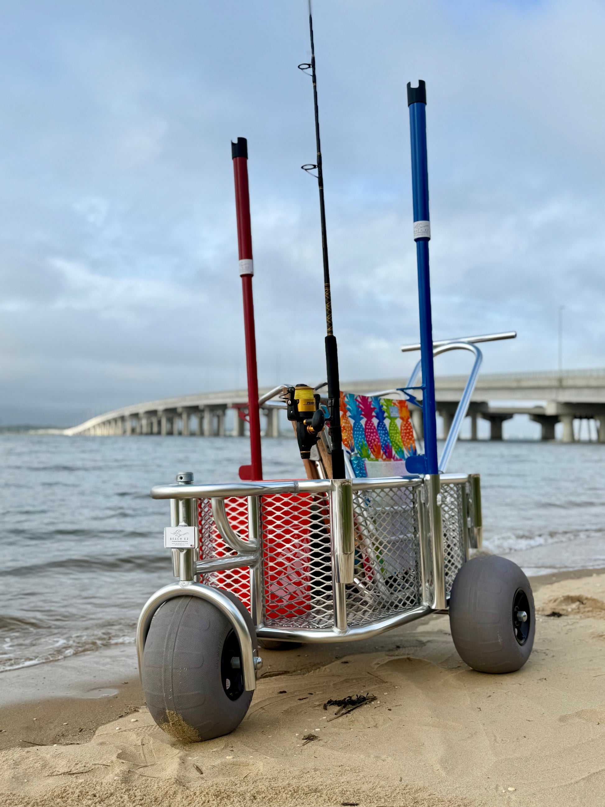 Angler surf fishing buggy, custom aluminum surf fishing cart with rod holders for fishing poles and space for beach gear. cart is full of gear and shows the surf fishing rod holders inserted into the beach buggy for easy transport across the sand.